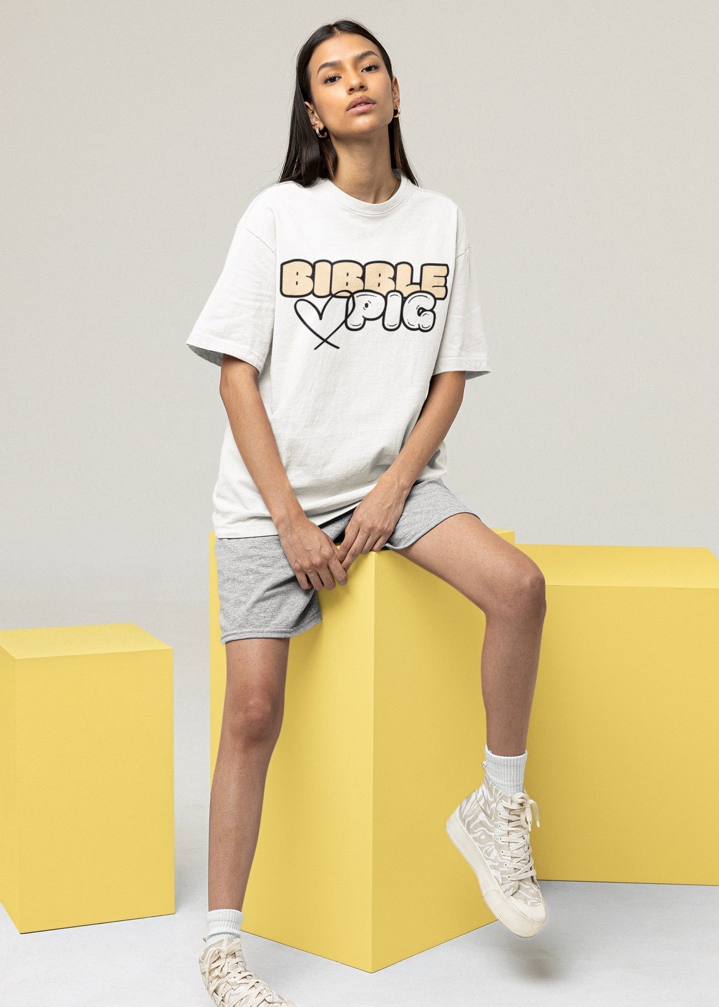 Model wearing white oversized t-shirt with large bold Bibble Pig logo with cute heart graphic.