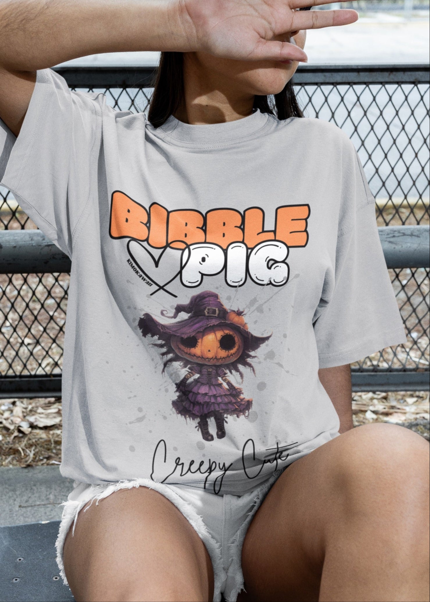 Close up of a model wearing grey oversized t-shirt featuring Pumpkin Willow Voodoo doll graphic and bold Bibble Pig Logo.
