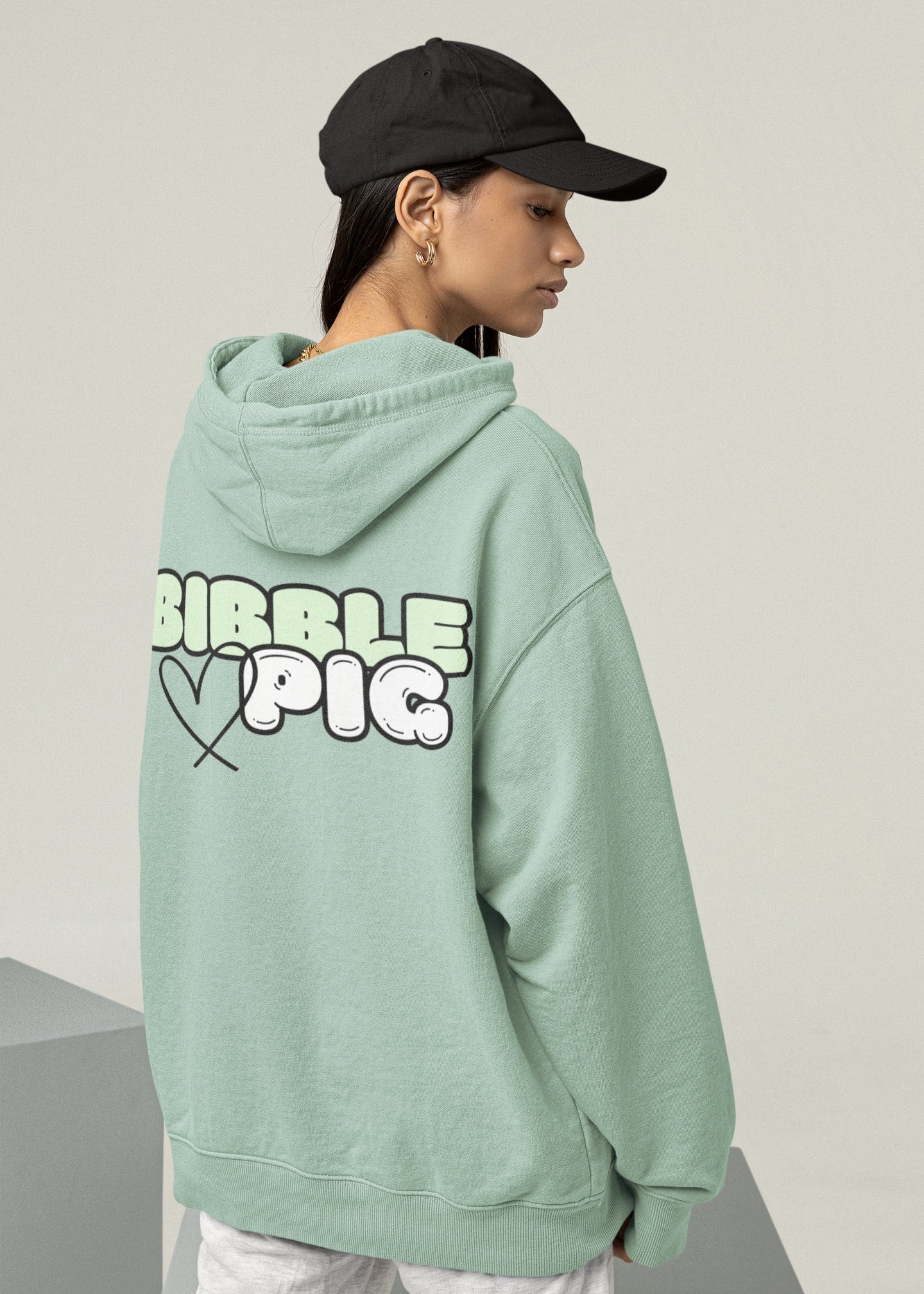 Model wearing a green oversized organic hoodie with our Pastel Green Bold Logo and cute heart design.