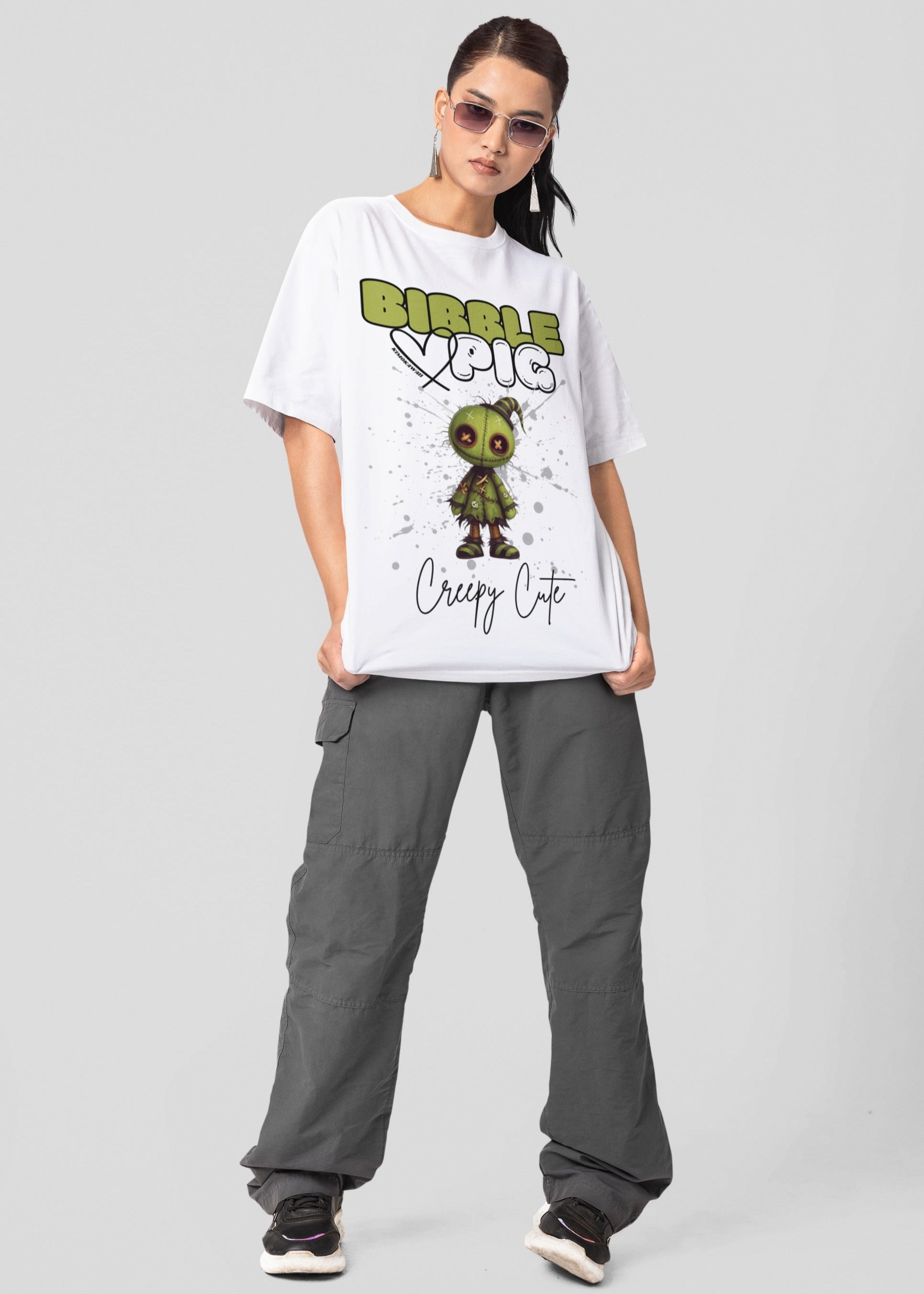 Model wearing white oversized t-shirt featuring Tattered Stitches Voodoo doll graphic and bold Bibble Pig Logo.  Paired with grey cargos and trainers for a chic streetwear style.