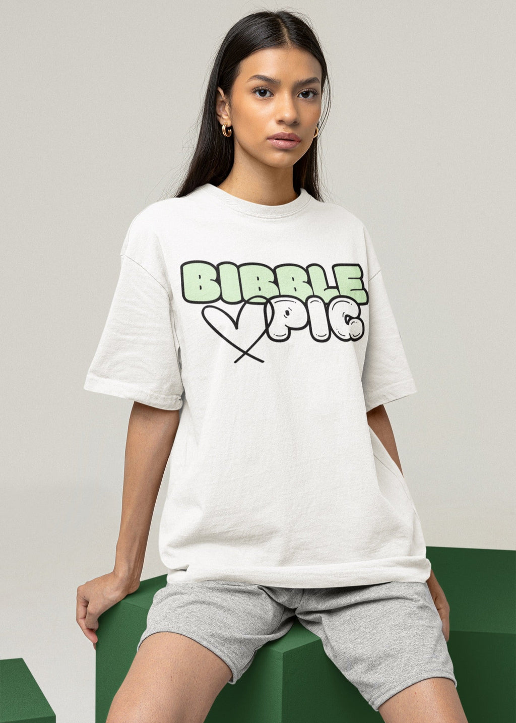 Model wearing Bibble Pig oversized organic cotton t shirt with pastel green logo and black heart design. Unisex UK streetwear fashion.