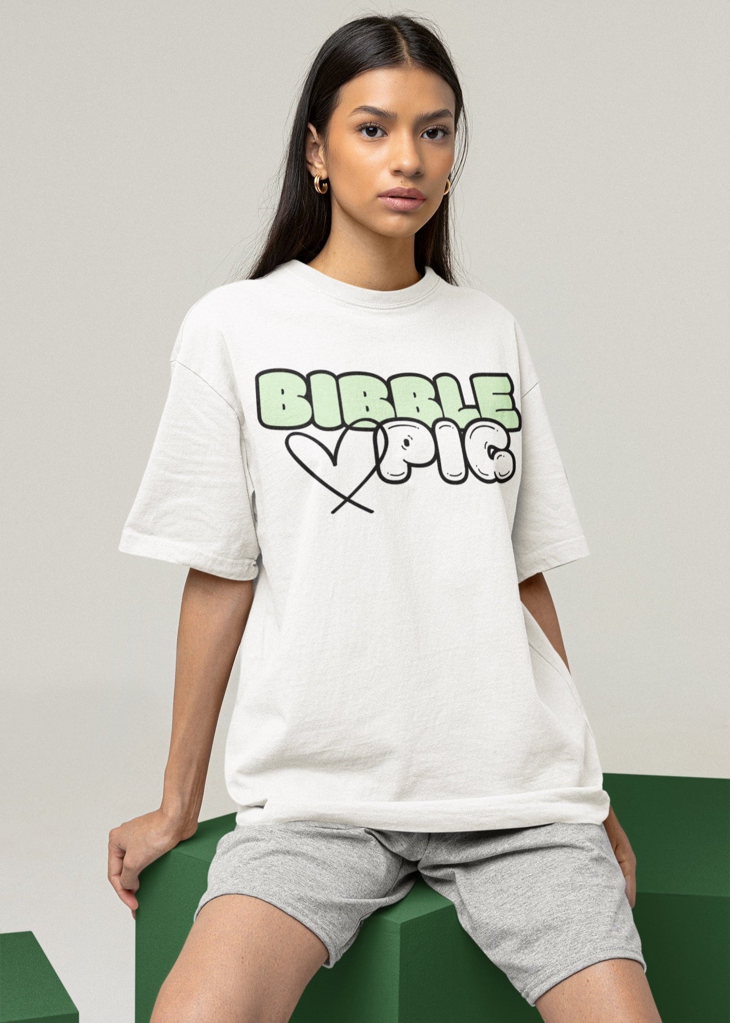 Model wearing Bibble Pig oversized organic cotton t shirt with pastel green logo and black heart design. Unisex UK streetwear fashion.